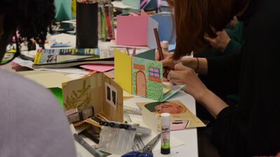 Workshop with people sitting at a table working on paper crafts and collaging