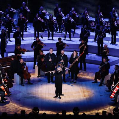 Aurora Orchestra perform on an illuminated stage; the members of the orchestra all wear black and have no music stands