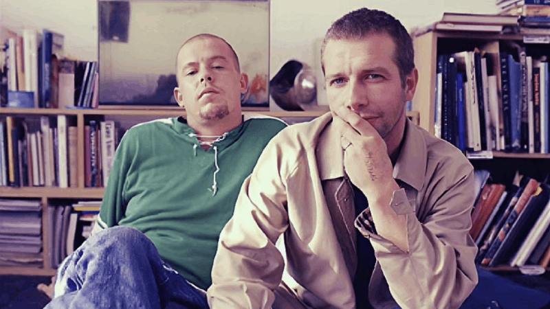 Fashion designer Lee Alexander McQueen and musician John Gosling sitting in the living room of a flat