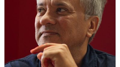 Anish Kapoor with his chin on his hand against a red background.