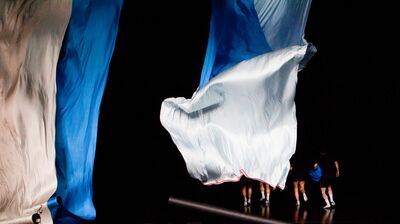 Four performers stand on a stage, covered by silk fabric