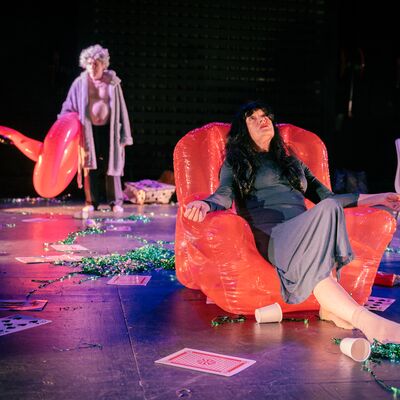 One performer sits in an inflatable chair on a stage, whilst another performer stands behind