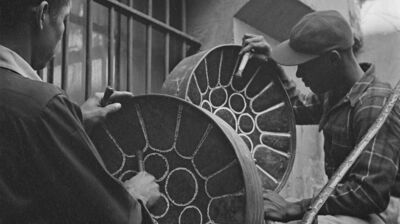 Black and white image of two young men tuning steel pans on a staircase