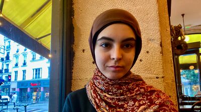A young woman wearing a red patterned scarf sitting in a cafe next to a window