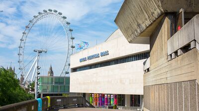 A concrete brutalist building with the London Eye and Big Ben in the background