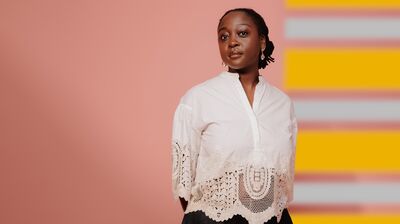 Cassie Kinoshi in a white lace blouse on a pink and yellow background facing the camera