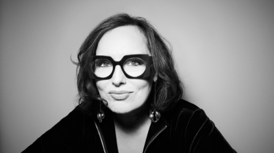 A black and white portrait of Deborah Frances White, a woman with dark hair and wearing glasses with a chunky frame