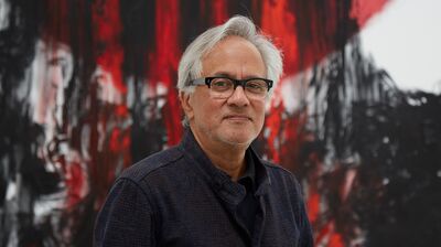 Anish Kapoor wearing glasses and a black suit, standing in front of a red and black artwork