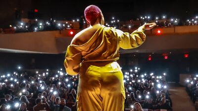 Performer in a gold outfit extends their hand to the audience at a theatre.