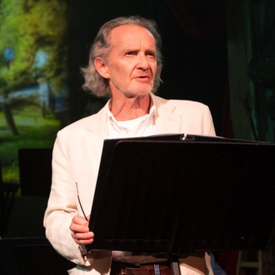 An actor wearing a white shirt, reading from a lectern.