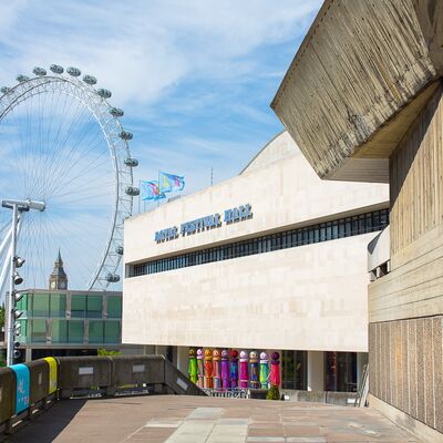 A concrete brutalist building with the London Eye and Big Ben in the background