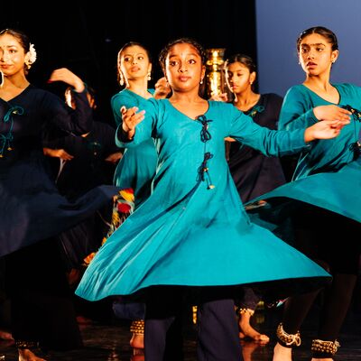 Young girls in vibrant blue tunics and bells around their ankles perform a traditional Indian dance on stage