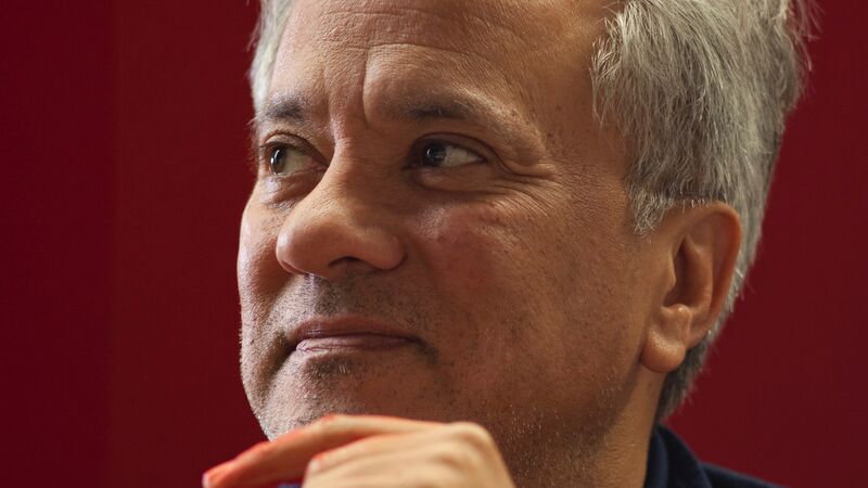 Anish Kapoor with his chin on his hand against a red background.