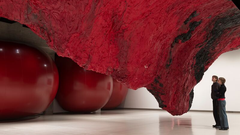 Two people looking at a massive Anish Kapoor red sculpture