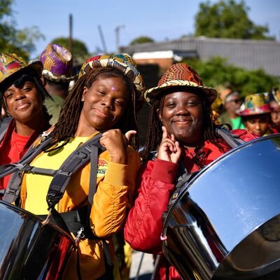 Members of Kinetika Bloco smiling while wearing harnesses holding steel pans