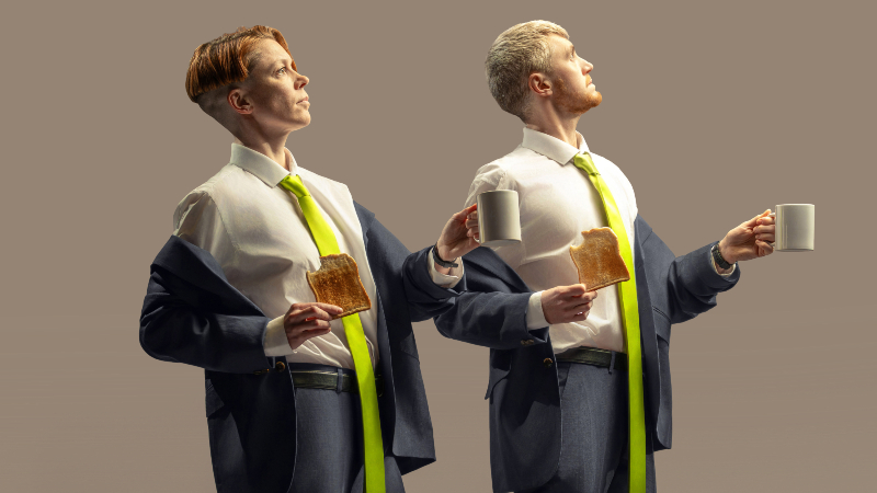 Two people wearing suits stand holding toast and mug