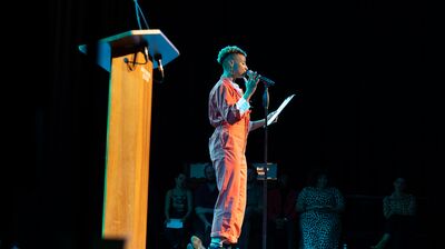 a poet performing on a stage in front of a lecturn.
