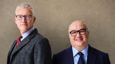 Hosts of The Rest is History standing against a beige background.
