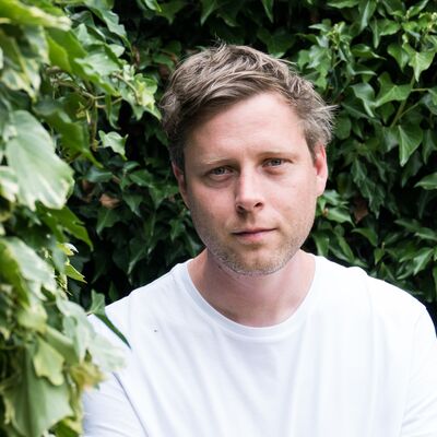 Max porter wears a white tshirt, with green leaves in the background.