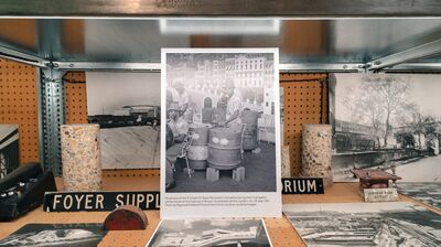 An archival display shelf featuring historical black and white photographs, concrete cylinders, and architectural signs.
