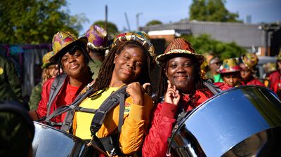 Members of Kinetika Bloco smiling while wearing harnesses holding steel pans
