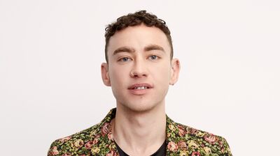 A man with short curly hair wearing a flower-patterned green suit
