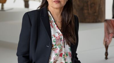 Bharti Kher wearing a black suit standing in a gallery.