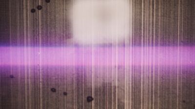 A fuzzy image of a rectangular object cut horizontally by a bright purple beam, with vertical lines and dark spots.
