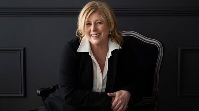 Liane Moriarty wearing a black jacket and white shirt against a black background