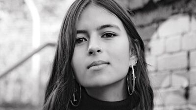 A black-and-white photo of a woman with long dark hair wearing a turtleneck jumper and big hoop earrings
