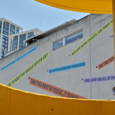 A large concrete building with colourful text decals affixed to its facade.