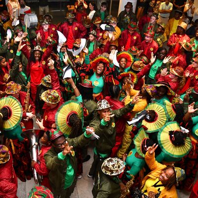 A large number of members of youth group Kinetika Bloco in bright clothing, some are playing instruments