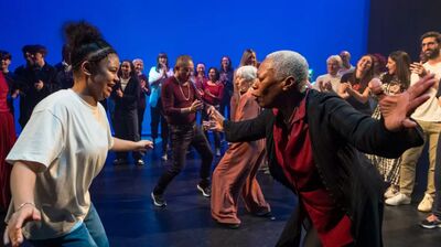 People of all ages dancing together in a large room with a blue background