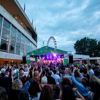 A crowd of people on the Riverside Terrace with the London Eye in the background