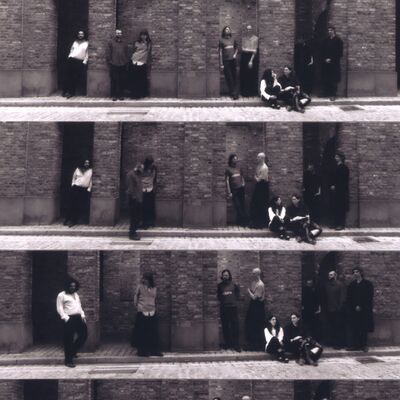 A black-and-white contact sheet of four vertical panels showing a group posing against a brick alcove wall.