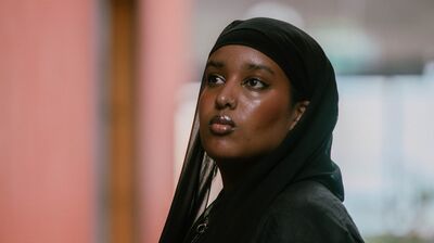 A three-quarter portrait of Momtaza Mehri looking upward, wearing a black hijab and matching black linen jacket.