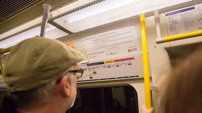 A man in a peaked cap reading a poem on a tube train
