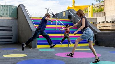 Three people jump over multicolored spots on the floor