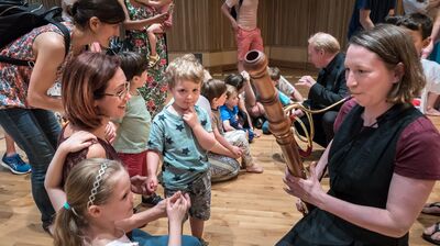 A musician kneeling and playing an instrument in front of a family.