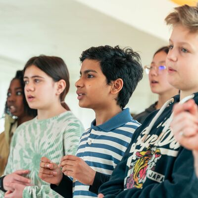A group of diverse children stand in a line singing or speaking during an interactive activity.
