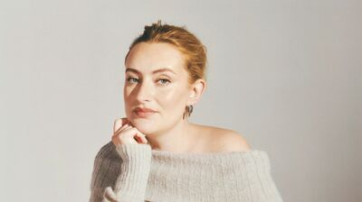 A lady in a beige jumper with her hair up resting her head on one hand.