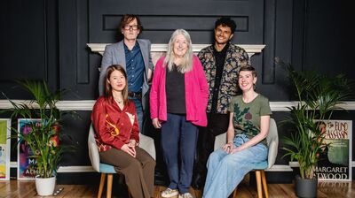 Five people posing for a photo in a room with wooden floors and navy walls