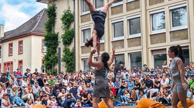 A crowd of people outside watching acrobats perform on a street