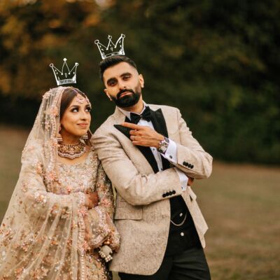 A man and woman in wedding clothes pose in a pastoral setting.