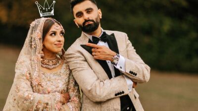 A man and woman in wedding clothes pose in a pastoral setting.