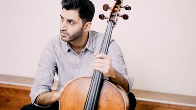 Soloist Kian Soltani, sitting holding his cello looking off to the side