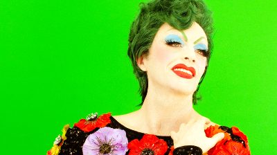 A drag performer with green hair posing on a bright green background.