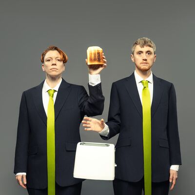 Two figures wearing suits stand next to each other, one holding a piece of toast and the other dropping a toaster