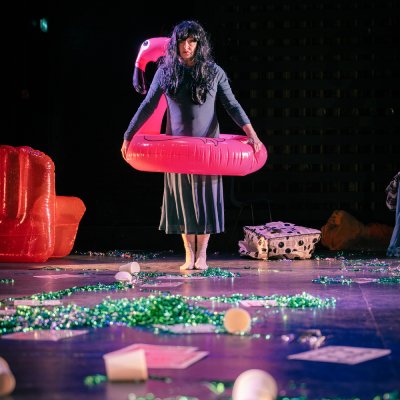 A figure stands on a stage holding a flamingo pool float