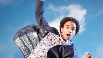 A person wearing a suit jacket and colourful flower shirt with their arms in the air and blue sky behind